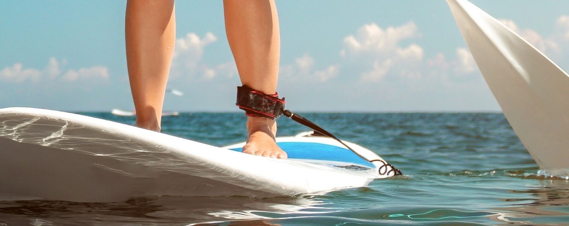 Person standing barefoot on a surfboard with ankle leash, gliding over blue ocean under a sunny sky